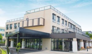 介護施設の建物外観。モダンな3階建てで、1階に広いエントランスと駐車スペースを備えている。